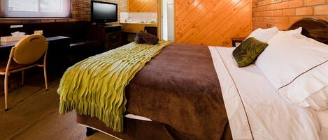 A bedroom with a bed, a desk, a chair, a television, and a brick wall.