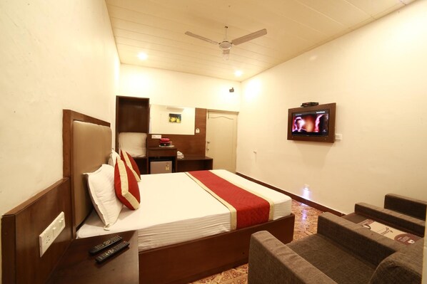 A hotel room with a bed, a television, a ceiling fan, and a small seating area.