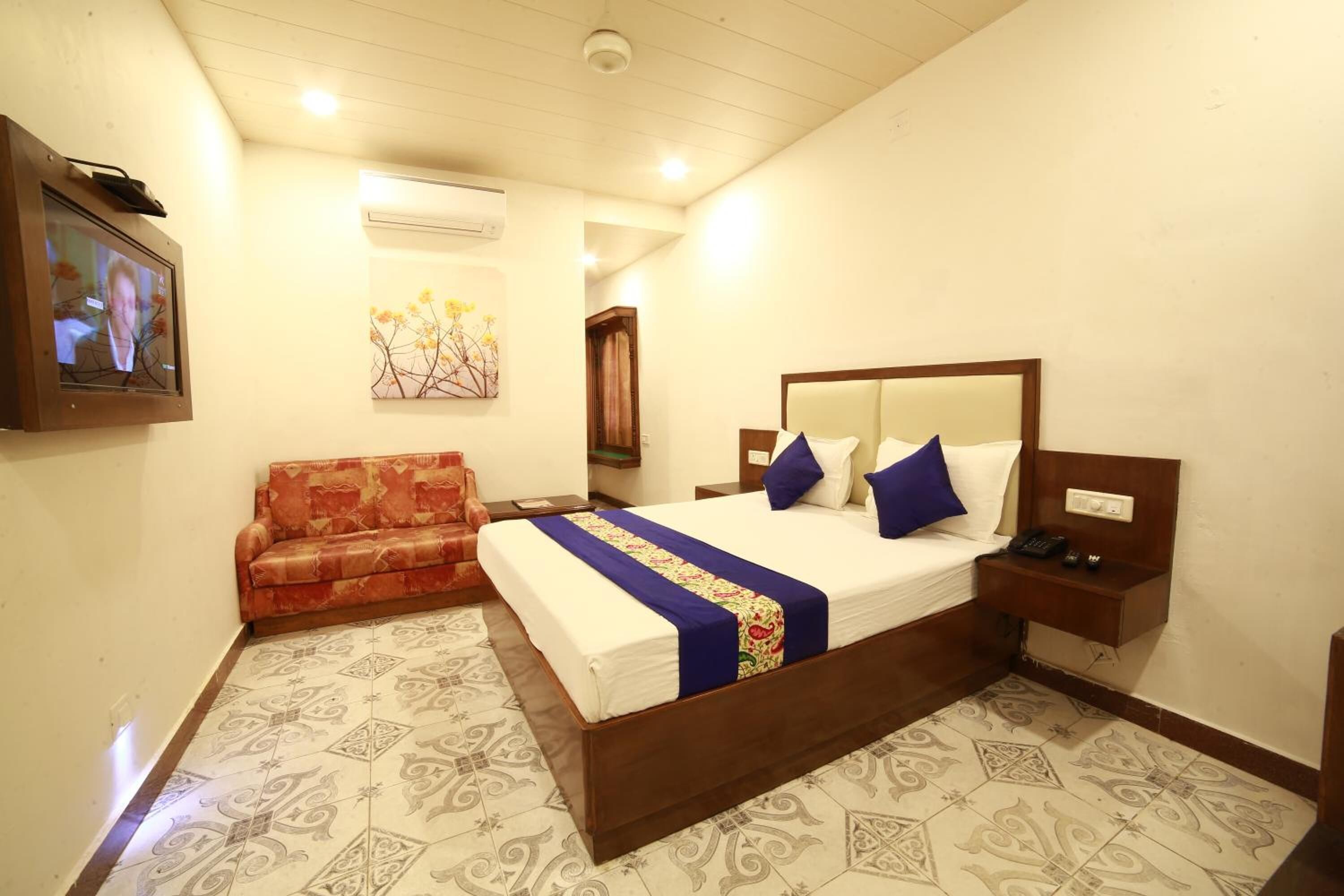 A hotel room with a bed, a sofa, a bedside table, and a wall-mounted TV.