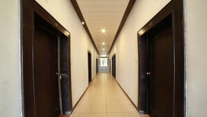Un pasillo largo y estrecho con puertas de madera oscura a ambos lados y suelo de baldosas.