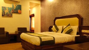 Una habitación de hotel con una cama grande, una mesita de noche, una silla y dos cuadros colgados en la pared.