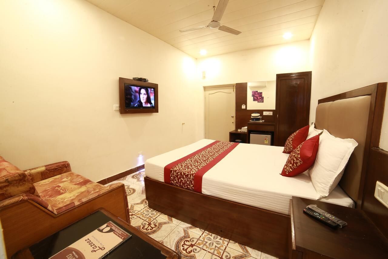 A hotel room with a bed, a TV mounted on the wall, a desk with a chair, and a bedside table with a remote control.