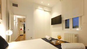 A hotel room with a bed, a TV mounted on the wall, a window with a view, and a breakfast tray on the bed.