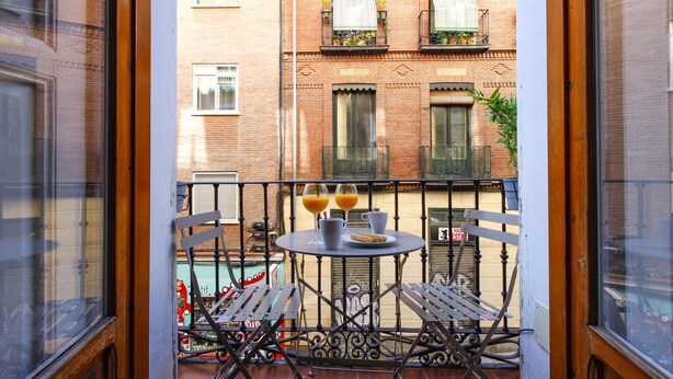 A balcony with a table set for two, featuring a pitcher, cups, and a plate of food.