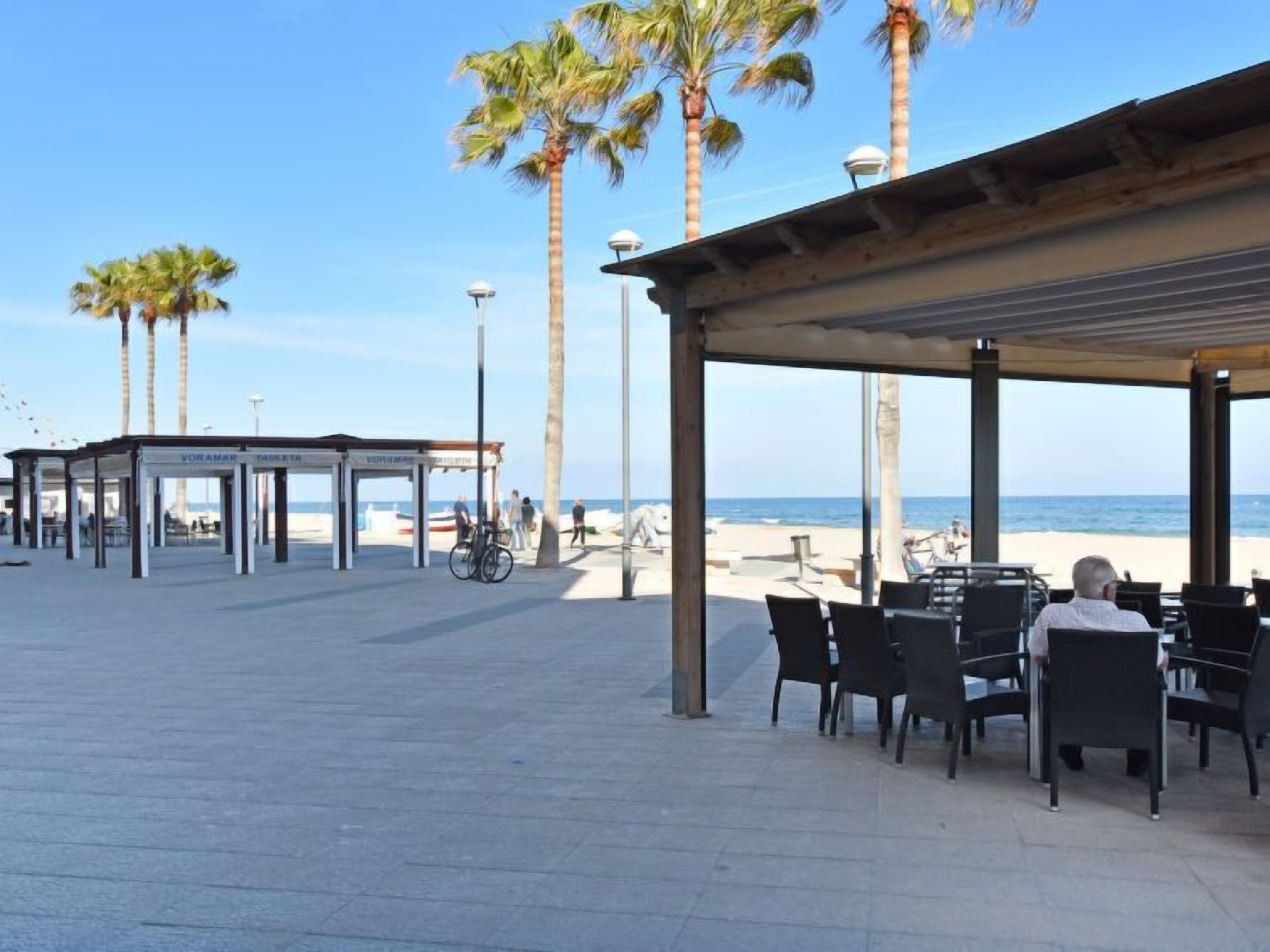 Un espace extérieur aménagé avec des tables et des chaises, une allée couverte et des palmiers.
