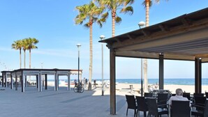 An outdoor seating area with tables and chairs, a covered walkway, and palm trees. - Magnolia by Interhome (Torredembarra)