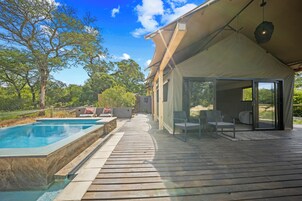 Una piscina con muelle de madera, zona de estar cubierta y vista a árboles.