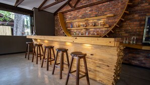 Una zona de bar con taburetes de madera, pared de ladrillo y estanterías con botellas.