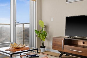 Una sala de estar moderna con un ventanal grande, una planta en maceta, un televisor de pantalla plana y una mesa de centro de vidrio.