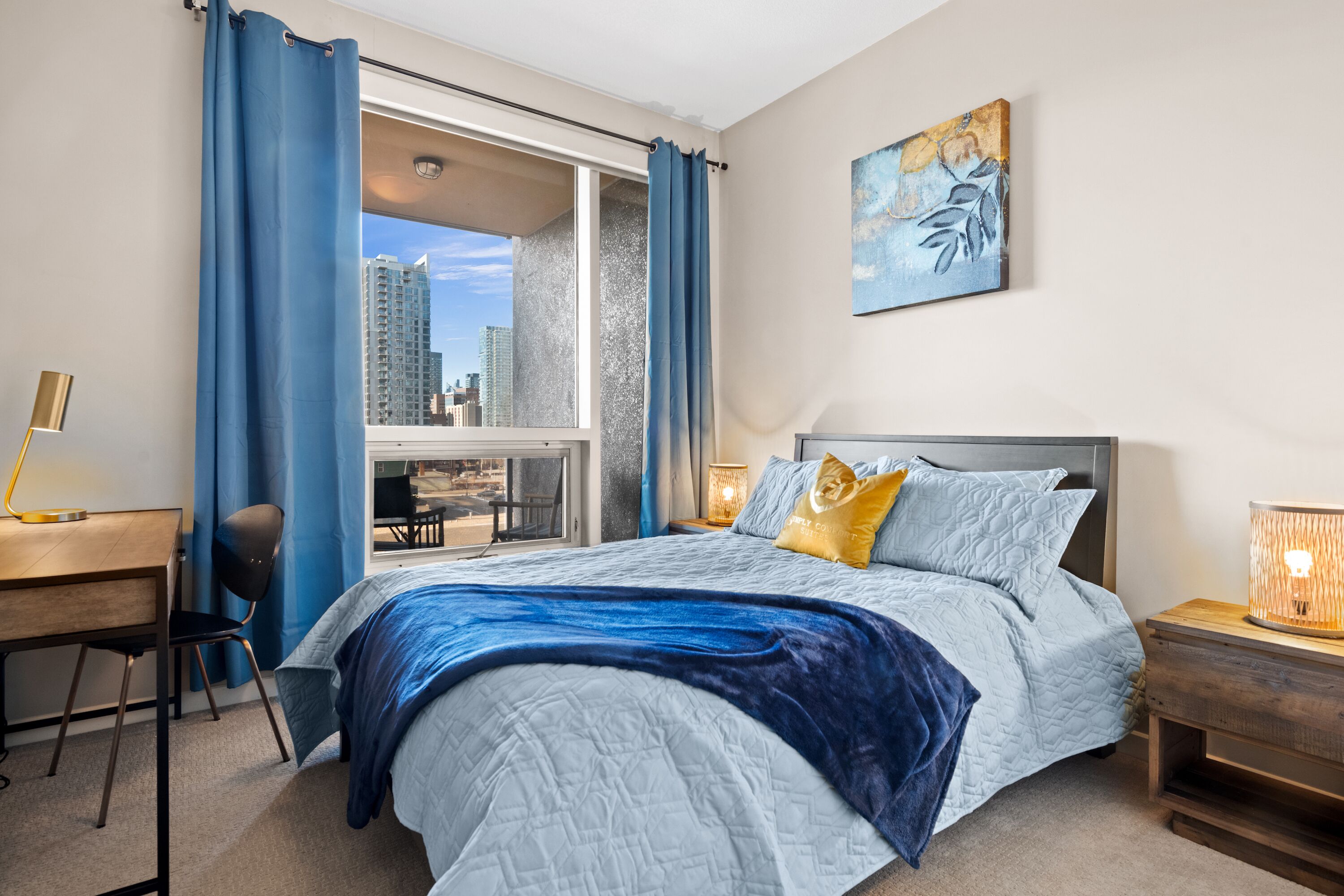 A bedroom with a large bed, a desk, a chair, and a window with curtains.