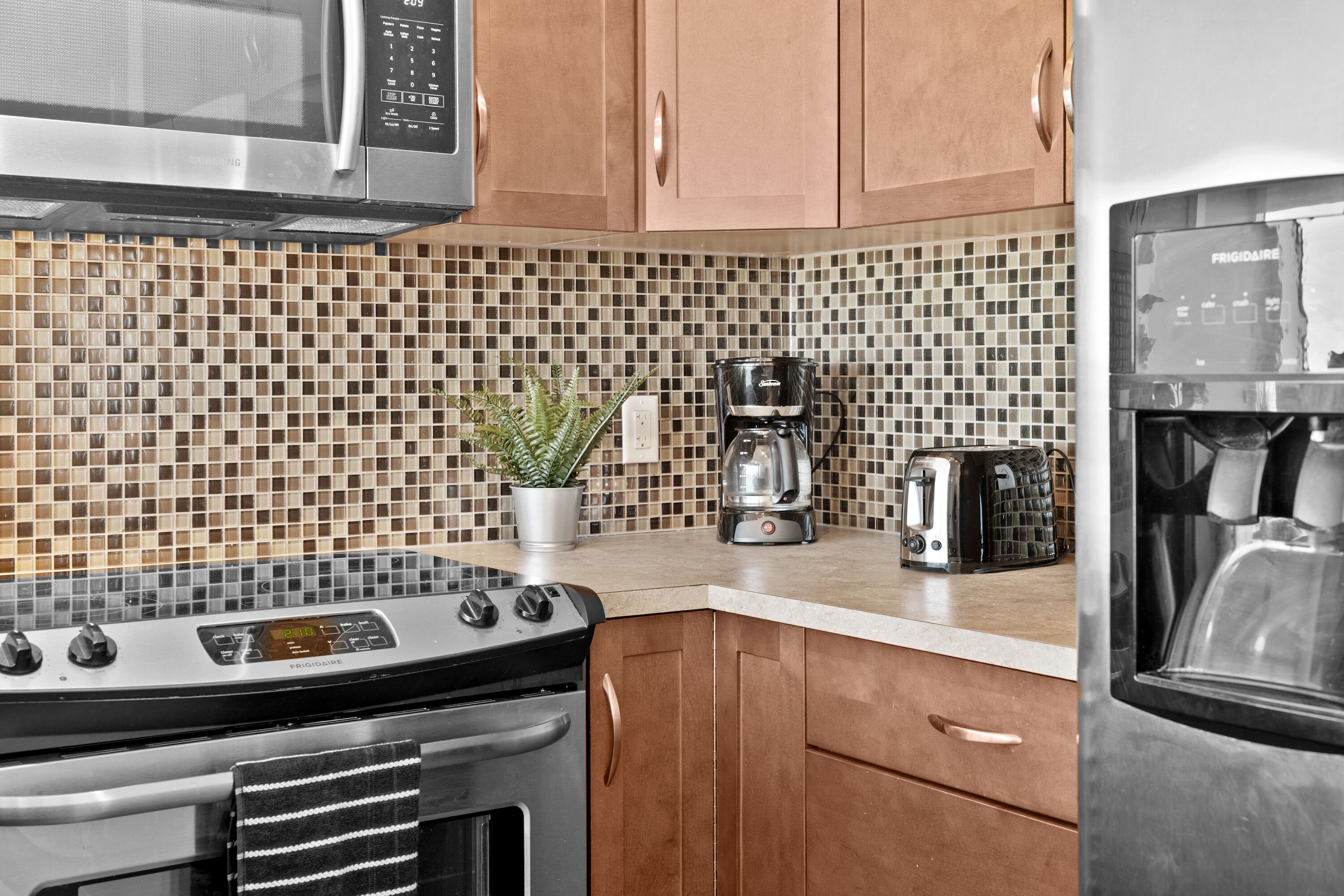 A kitchen with a microwave, stove, coffee maker, toaster, and refrigerator.