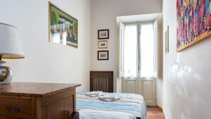 Een slaapkamer met een bed, een houten bureau, een lamp en een raam met gordijnen.