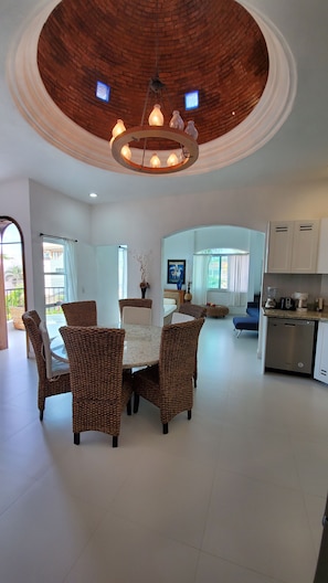 Enjoy meals in the central dining area with a round table and wicker chairs, offering a view of the outdoors.