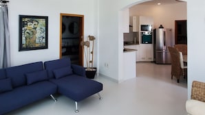 A living room with a blue sectional sofa, a white armchair, a ceiling with a brick design, and a kitchen in the background. - Spacious modern apartment Golden Zone 2F (Bucerias)