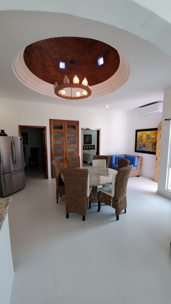 A spacious living area with a round dining table surrounded by wicker chairs, a modern kitchen with a refrigerator, and a cozy seating area with a blue sofa. - Spacious modern apartment Golden Zone 2F (Bucerias)