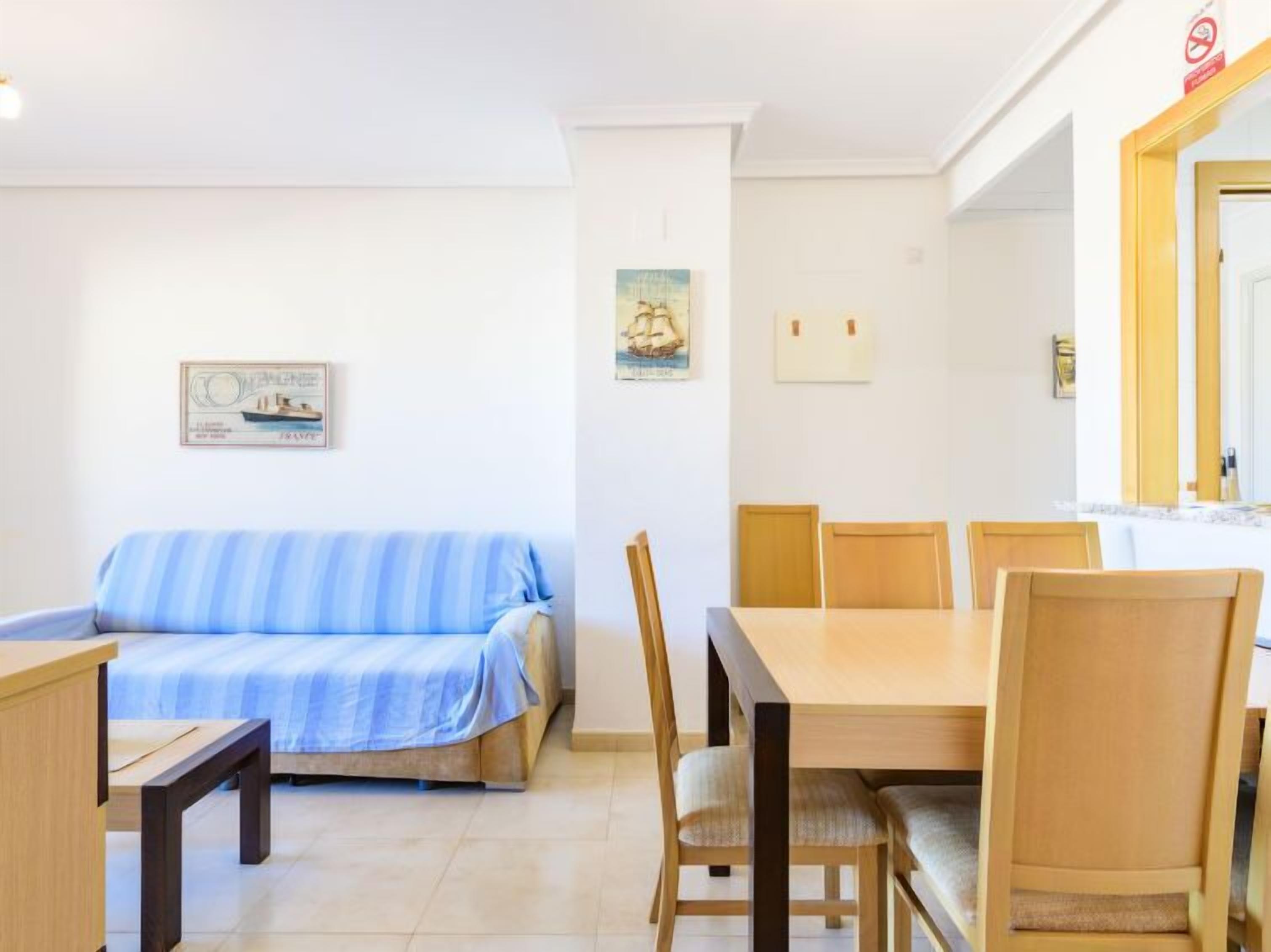 A room with a blue-striped sofa, a wooden dining table with four chairs, and a small wooden desk.