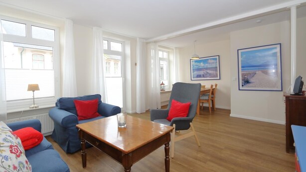 A spacious living room with a wooden coffee table, blue sofas, and a grey armchair. - Möwennest, Germany (Sylt)