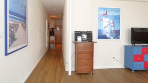 A hallway with a wooden floor, a small kitchenette, a wooden dresser, and a TV stand with a flat-screen TV. - Möwennest, Germany (Sylt)