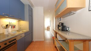 A narrow kitchen with blue cabinets, a stove, and a coffee maker on the counter. - Möwennest, Germany (Sylt)