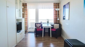 A compact room with a television on a cabinet, a small dining table with two chairs, and a window with curtains. - House by the sea 139a, Germany (Sylt)