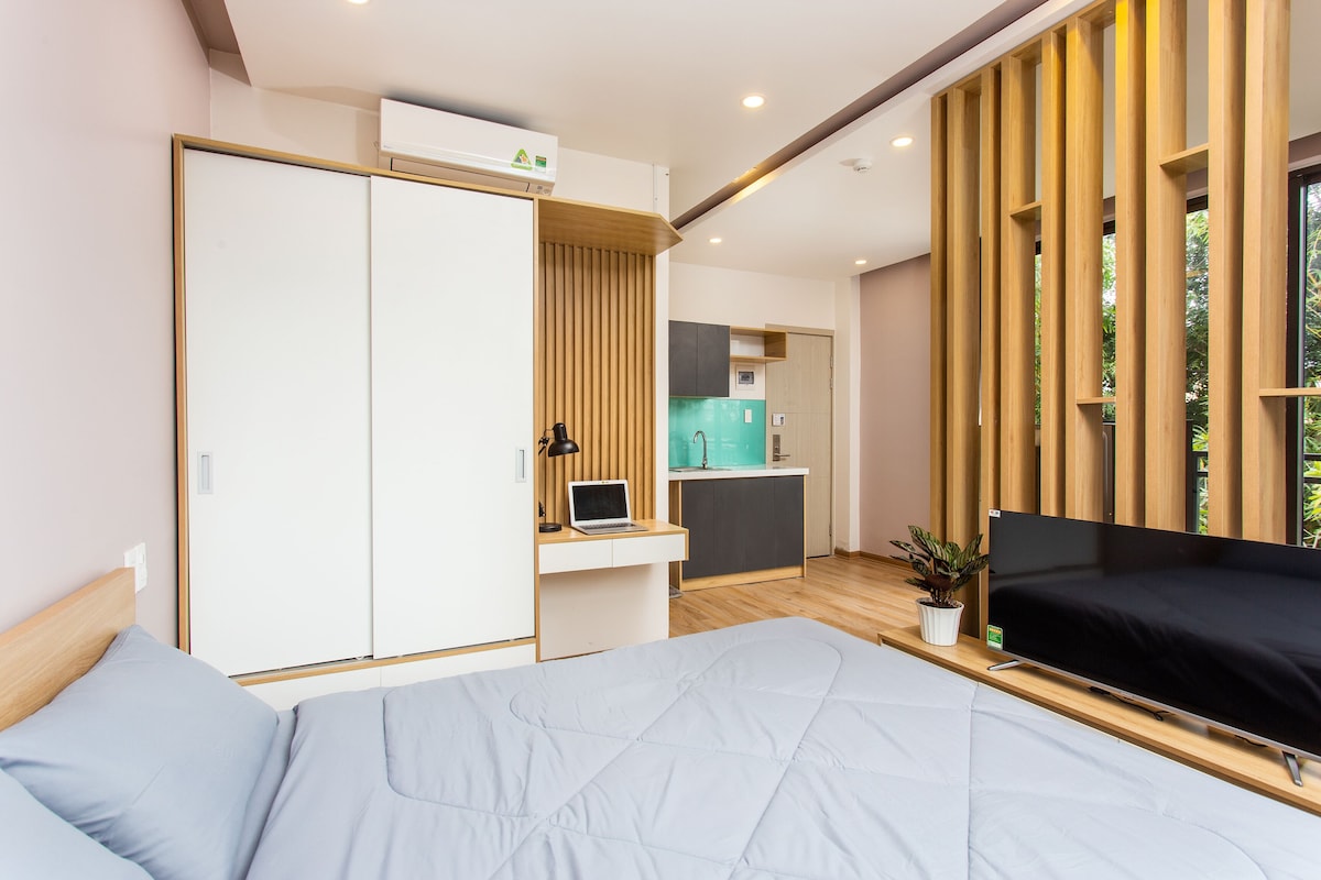 A modern bedroom with a bed, a desk with a laptop, a TV, and a wardrobe.