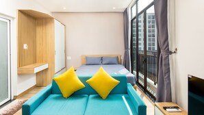 Una camera d'hotel moderna con un letto grande, un divano con cuscini gialli, una parete rivestita in legno e vista sulla città attraverso ampie finestre.