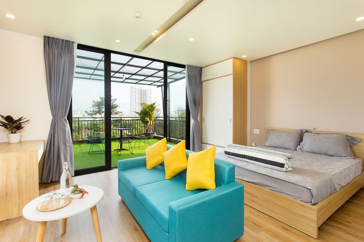 A modern hotel room with a sofa, bed, and a balcony with a view of the city.