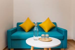 A blue sofa with yellow pillows, a clear glass bottle, and two small jars on a white round table.