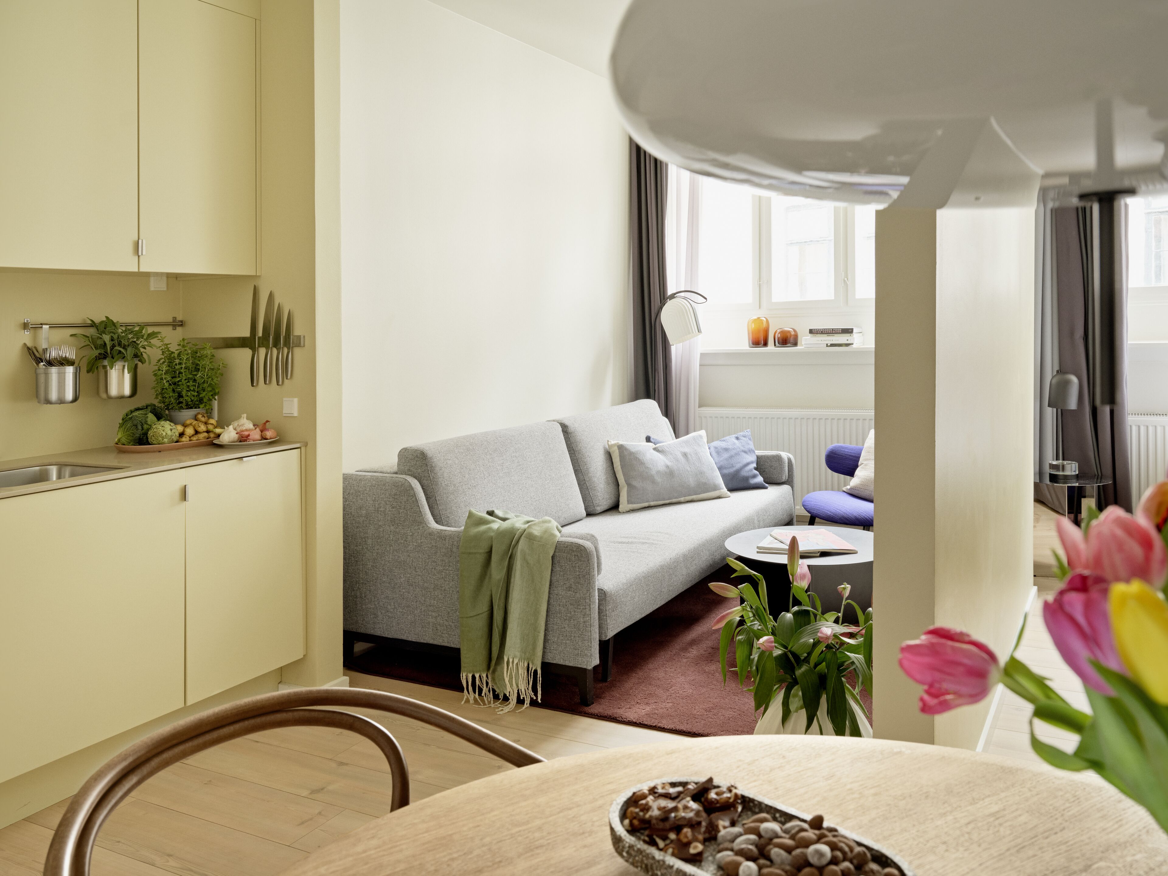 A modern living room with a grey sofa, a small round table, and a dining area with a wooden chair.