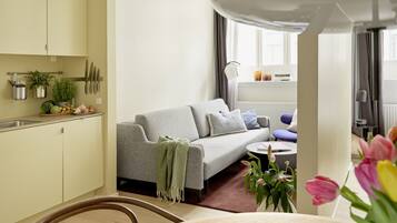 A modern living room with a grey sofa, a small round table, and a dining area with a wooden chair.