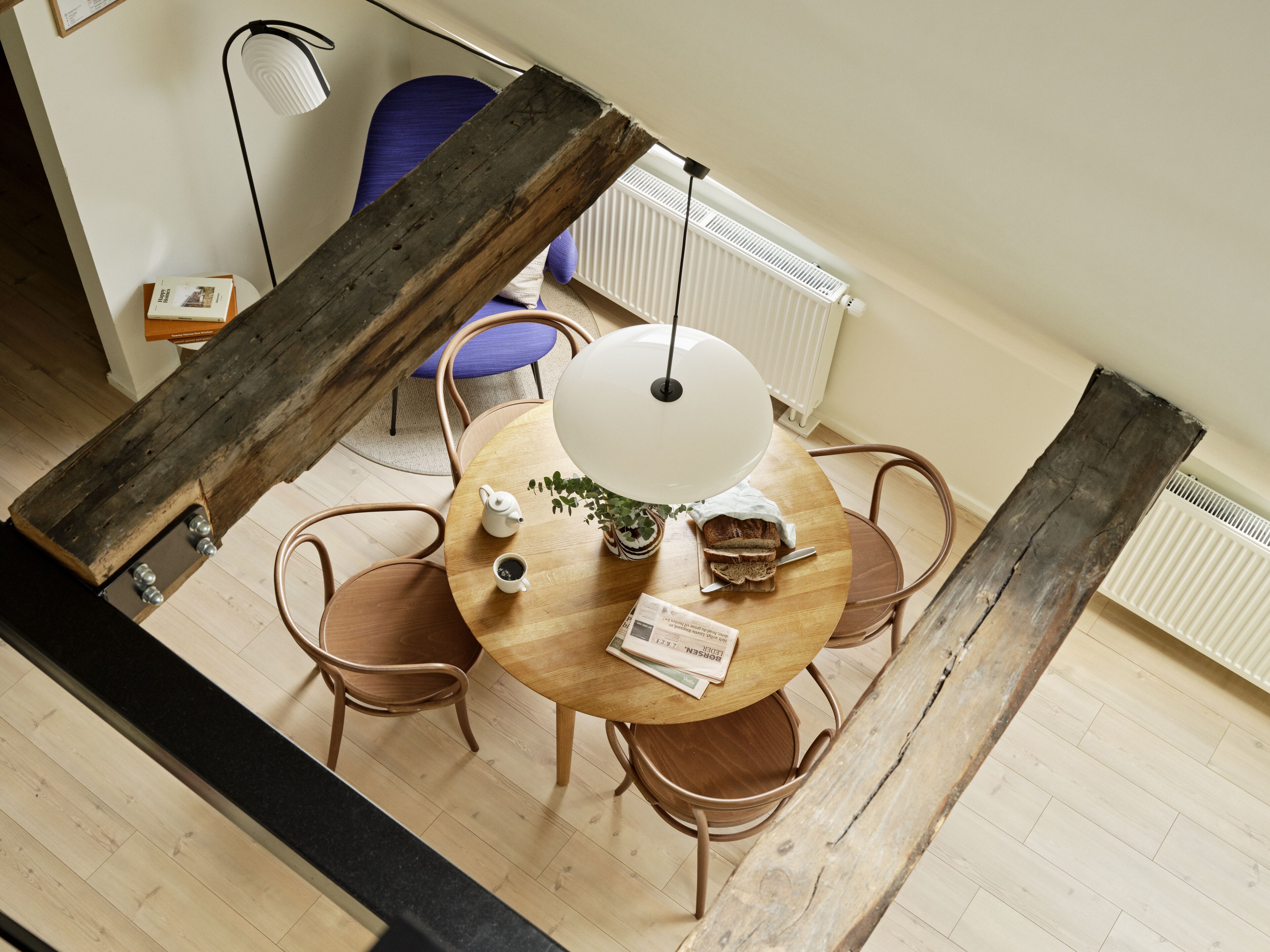 A dining area with a round wooden table, four chairs, a white table lamp, and a radiator in the background.