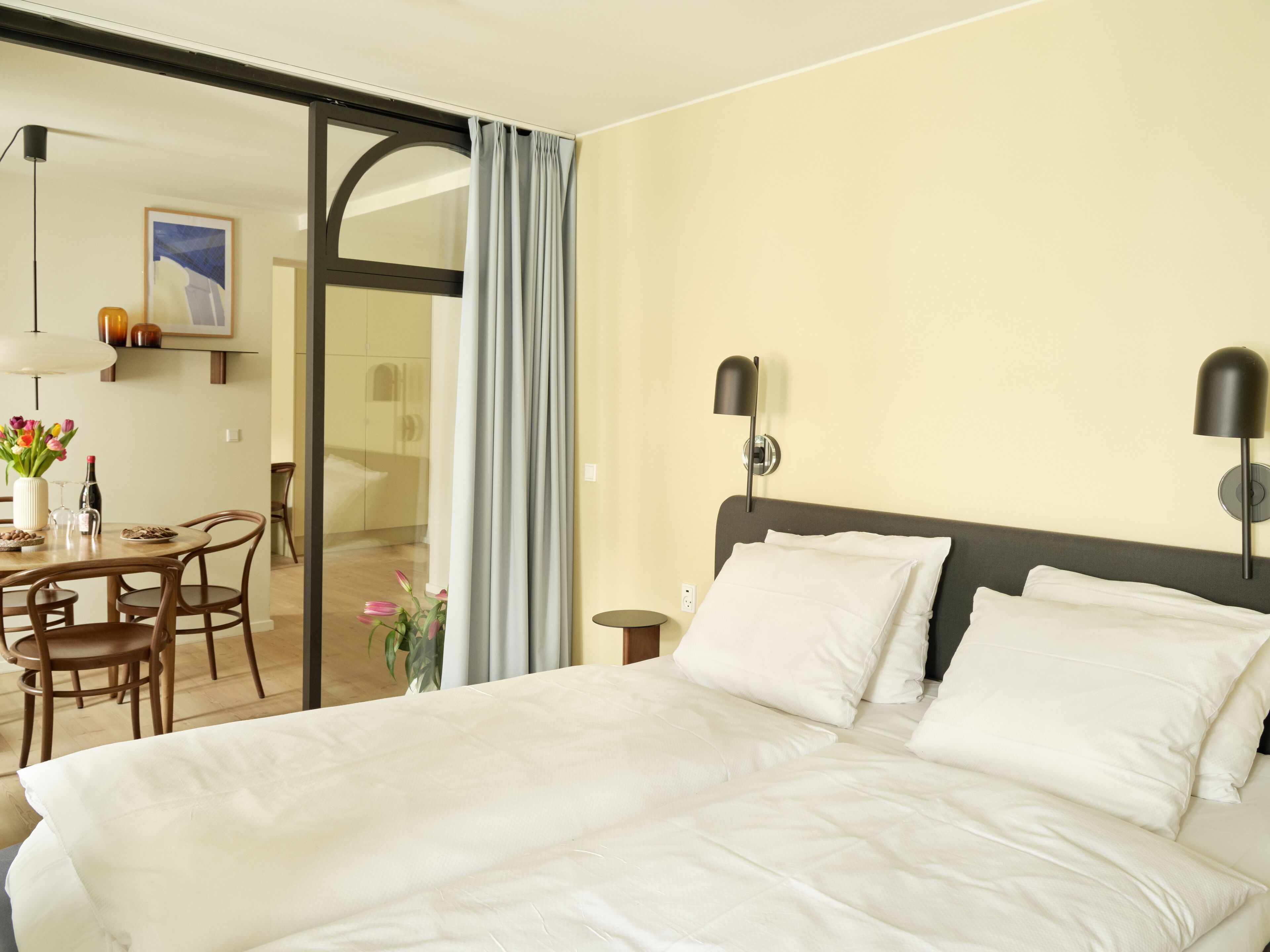 Habitación de hotel con cama, escritorio y sillas, una mesa con flores y un cuadro en la pared.