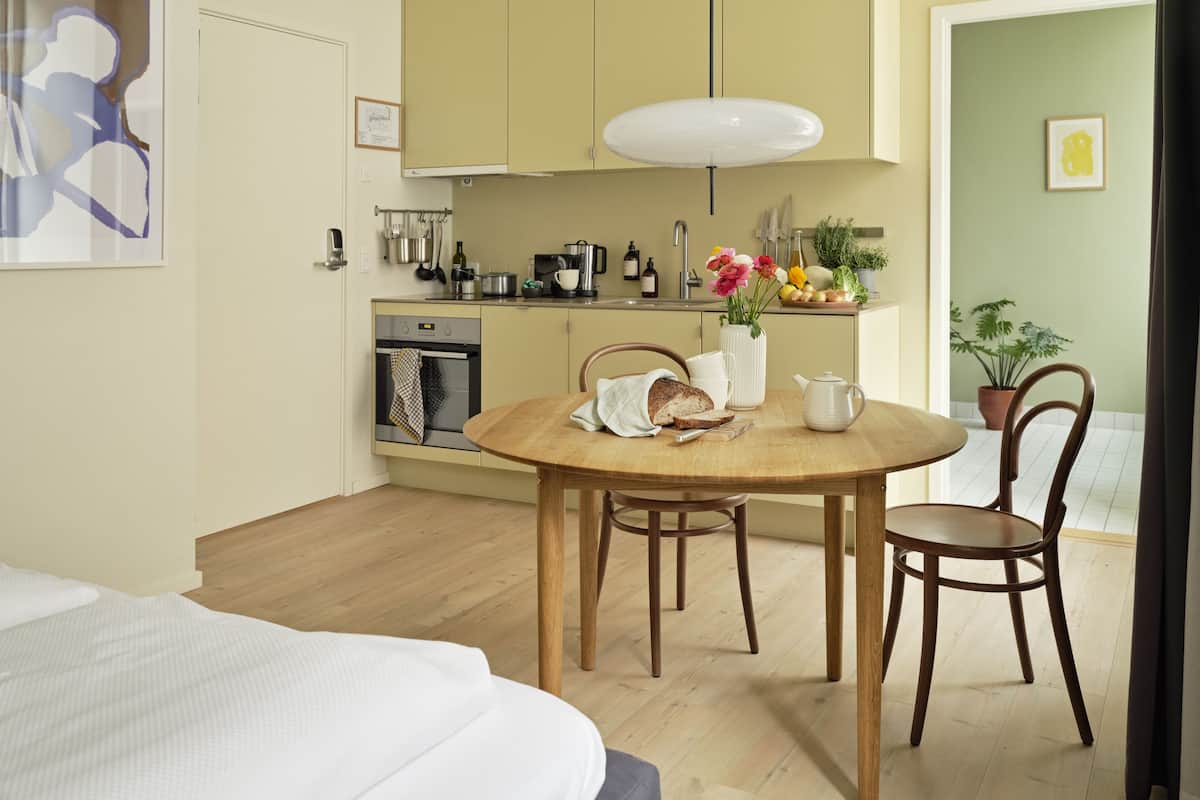 Une cuisine compacte dotée d’appareils électroménagers modernes, une table à manger avec des chaises, et un lit au premier plan.