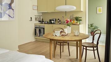 A compact kitchen with modern appliances, a dining table with chairs, and a bed in the foreground.