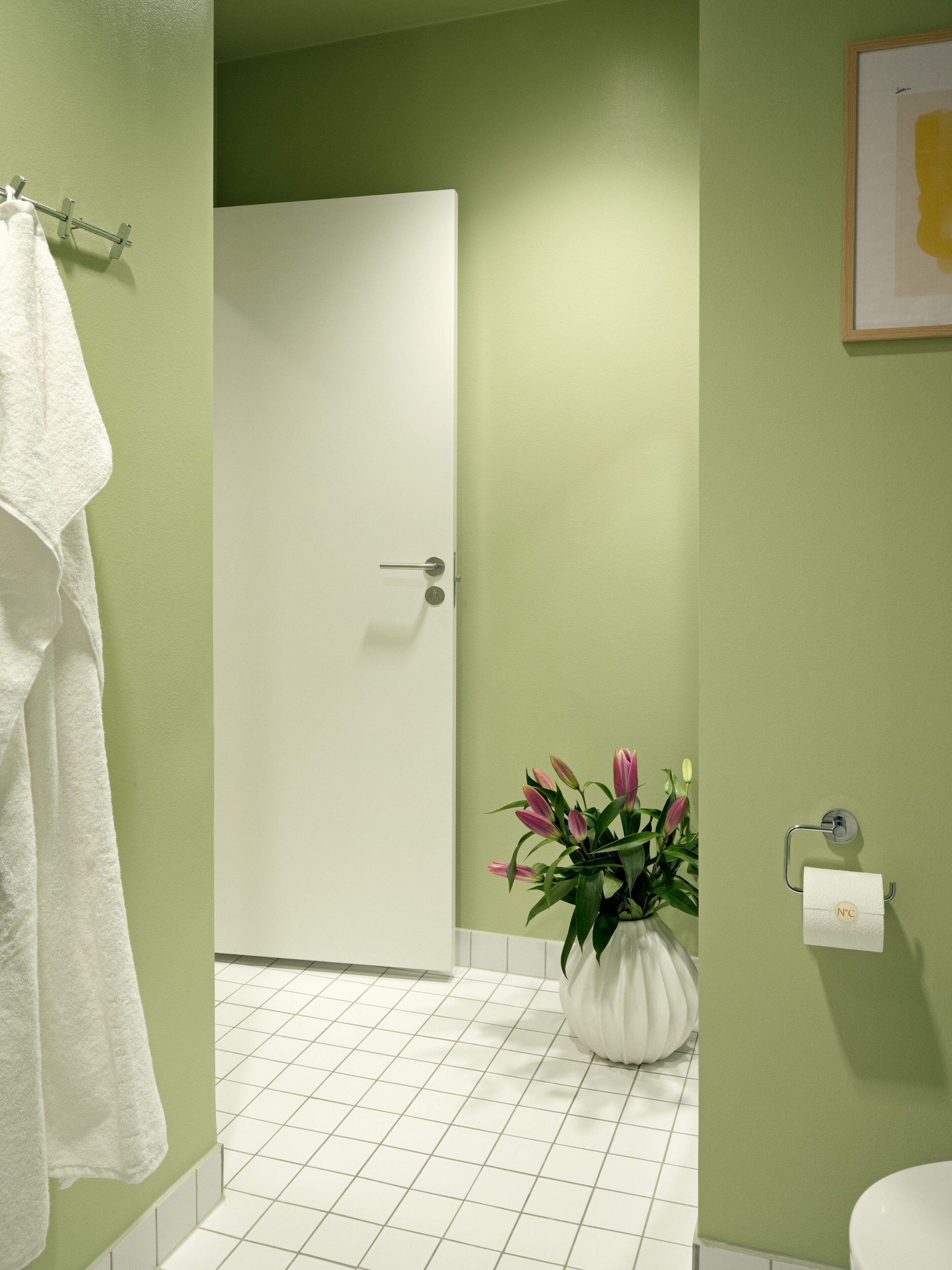 Ein Badezimmer mit grünen Wänden, einer weißen Tür, einer weißen Toilette, einem weißen Waschbecken und einem weißen Handtuchhalter.