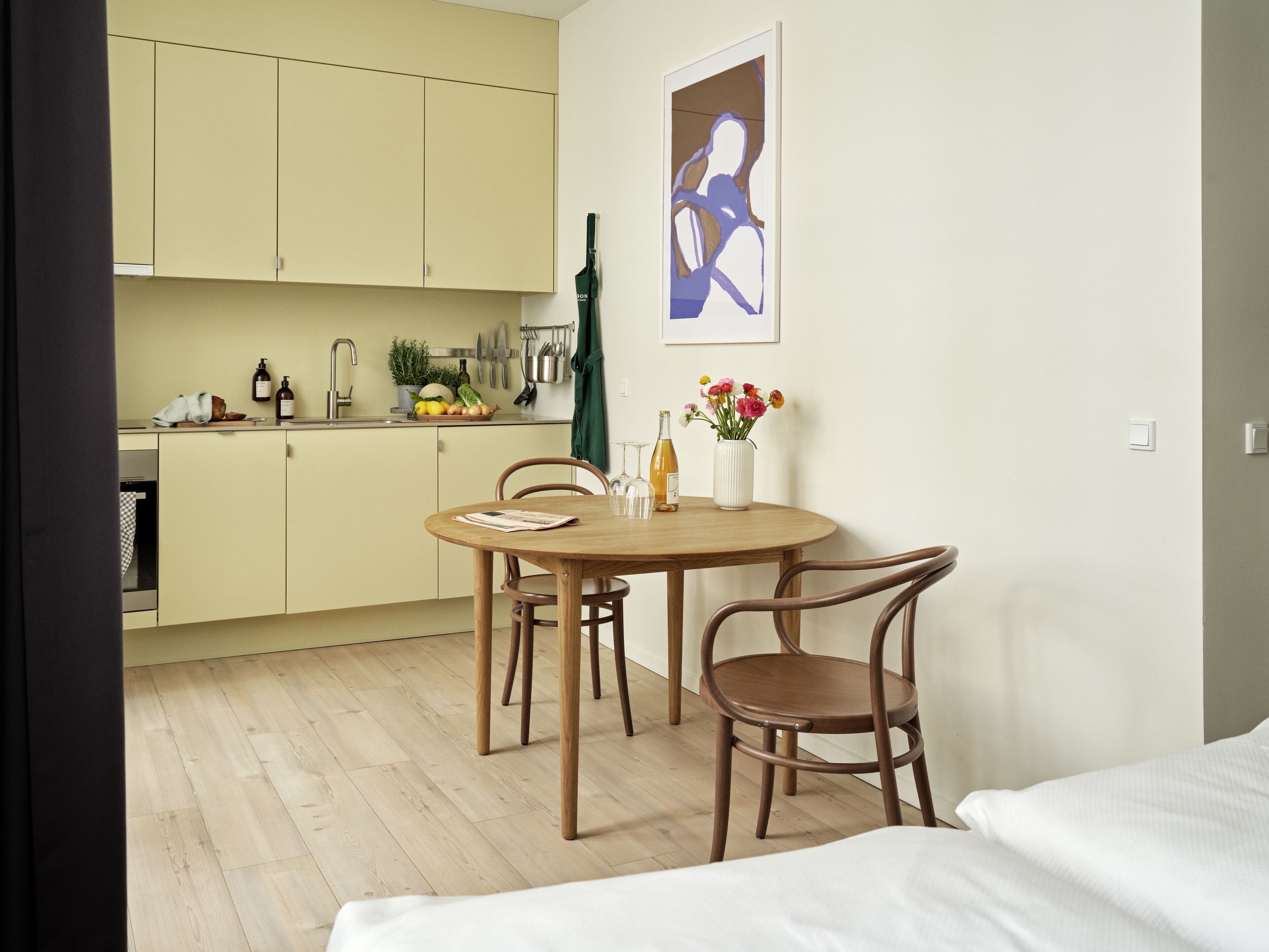 Eine kleine Küche mit Essbereich, Holzkohlenstühle, ein Tisch und ein Bett mit weißer Bettwäsche.