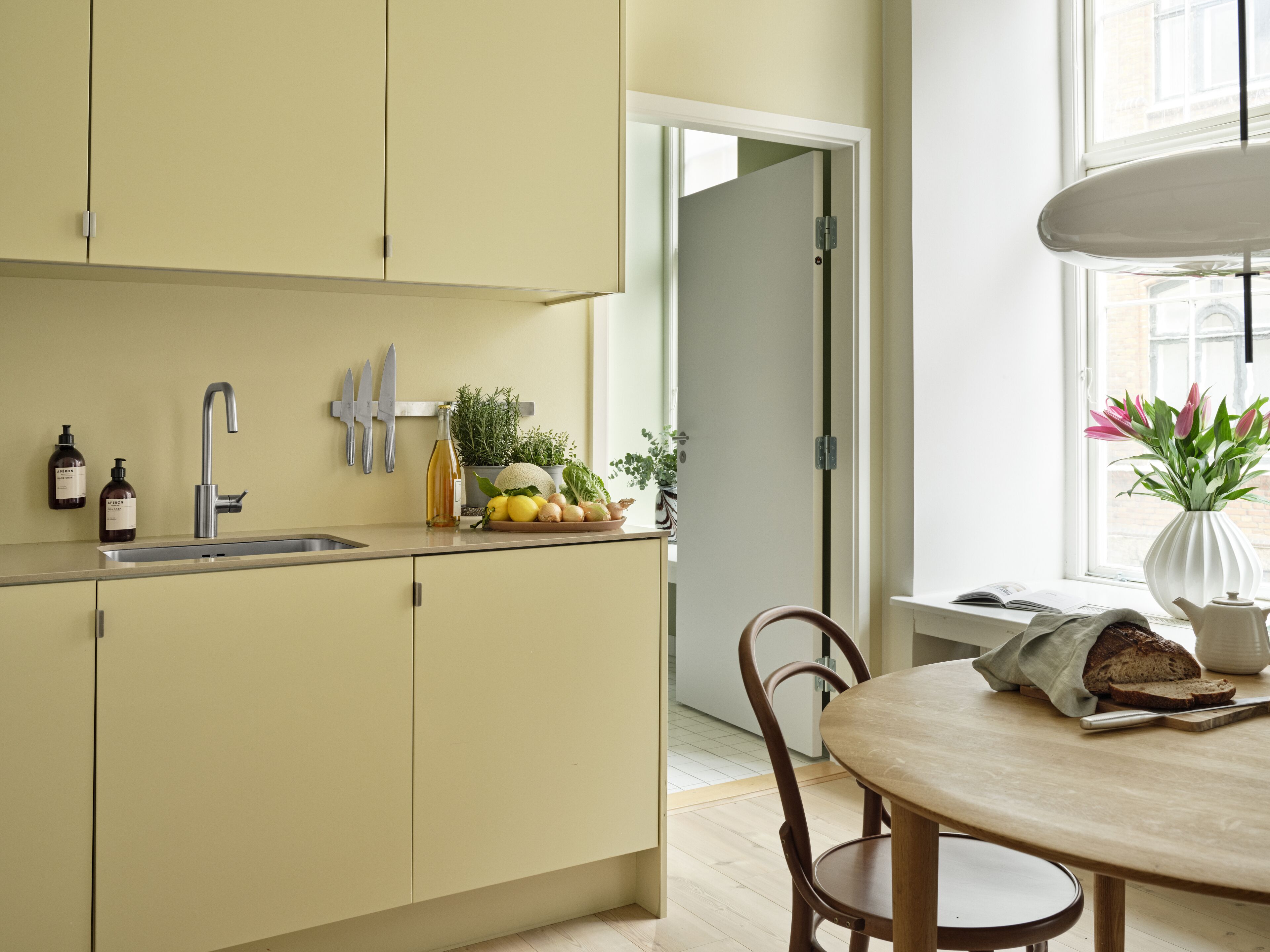 A modern kitchen with a sink, faucet, and cabinets. There is a window with a view of buildings outside.