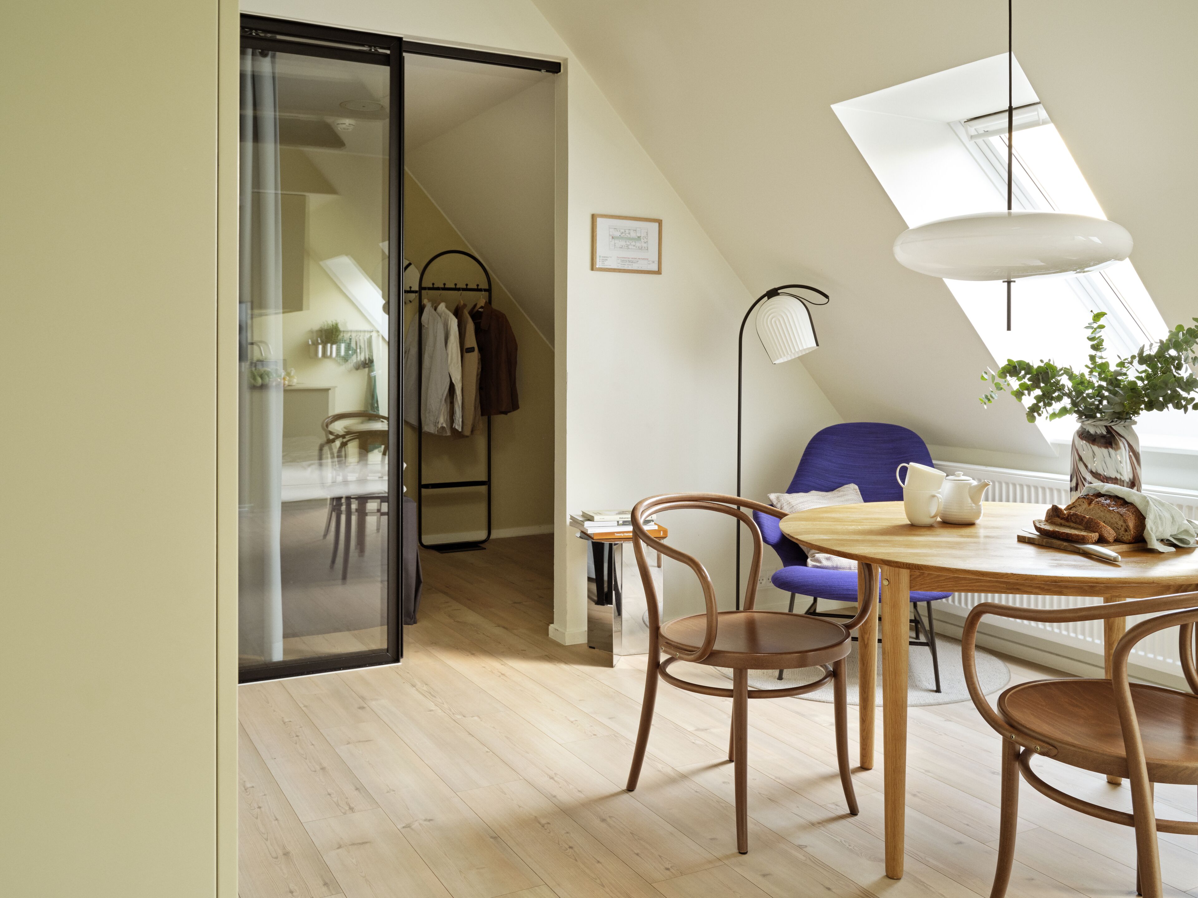 Een moderne loft slaapkamer met een groot dakvenster, een eethoek met houten meubels en uitzicht op de stad.