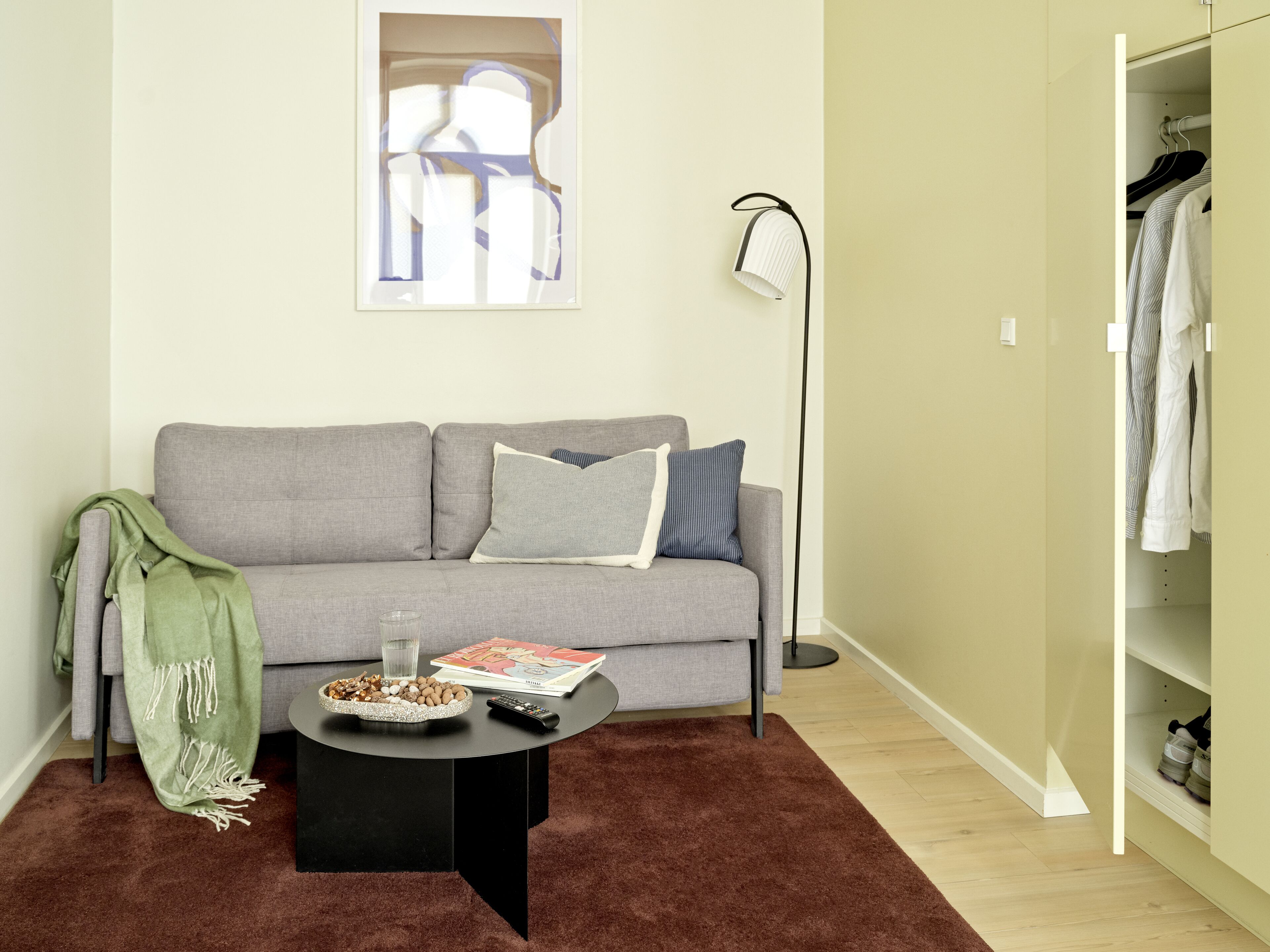 Una sala de estar moderna con un sofá gris, una mesa de centro con aperitivos, una lámpara de pie y un armario.
