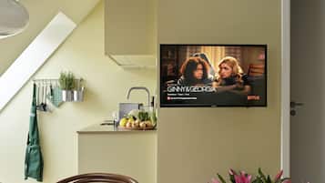 Une cuisine moderne avec un coin repas, un téléviseur diffusant la série « GINNY & GEORGIA » sur Netflix, et un vase rempli de fleurs roses.