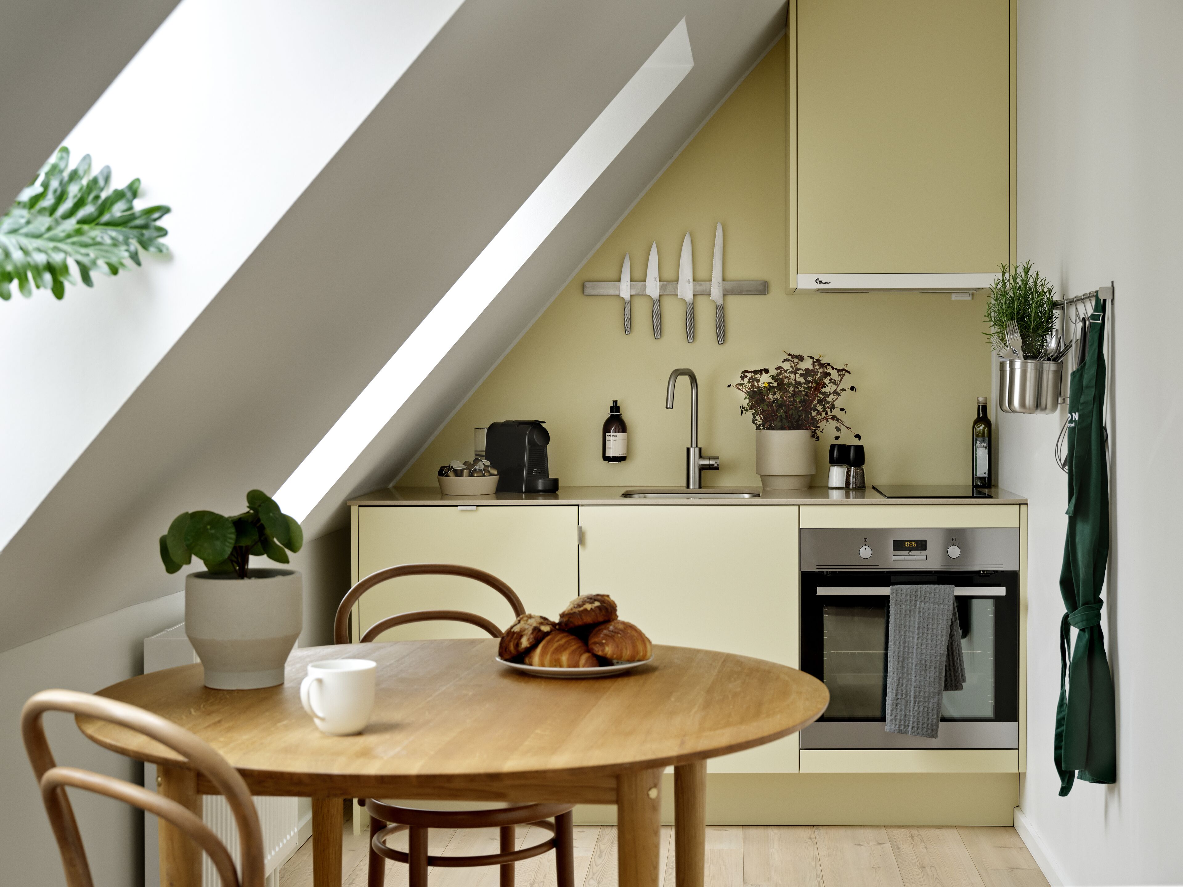 Una cocina moderna con un tragaluz, una mesa de comedor con sillas, una cafetera y una planta en maceta.