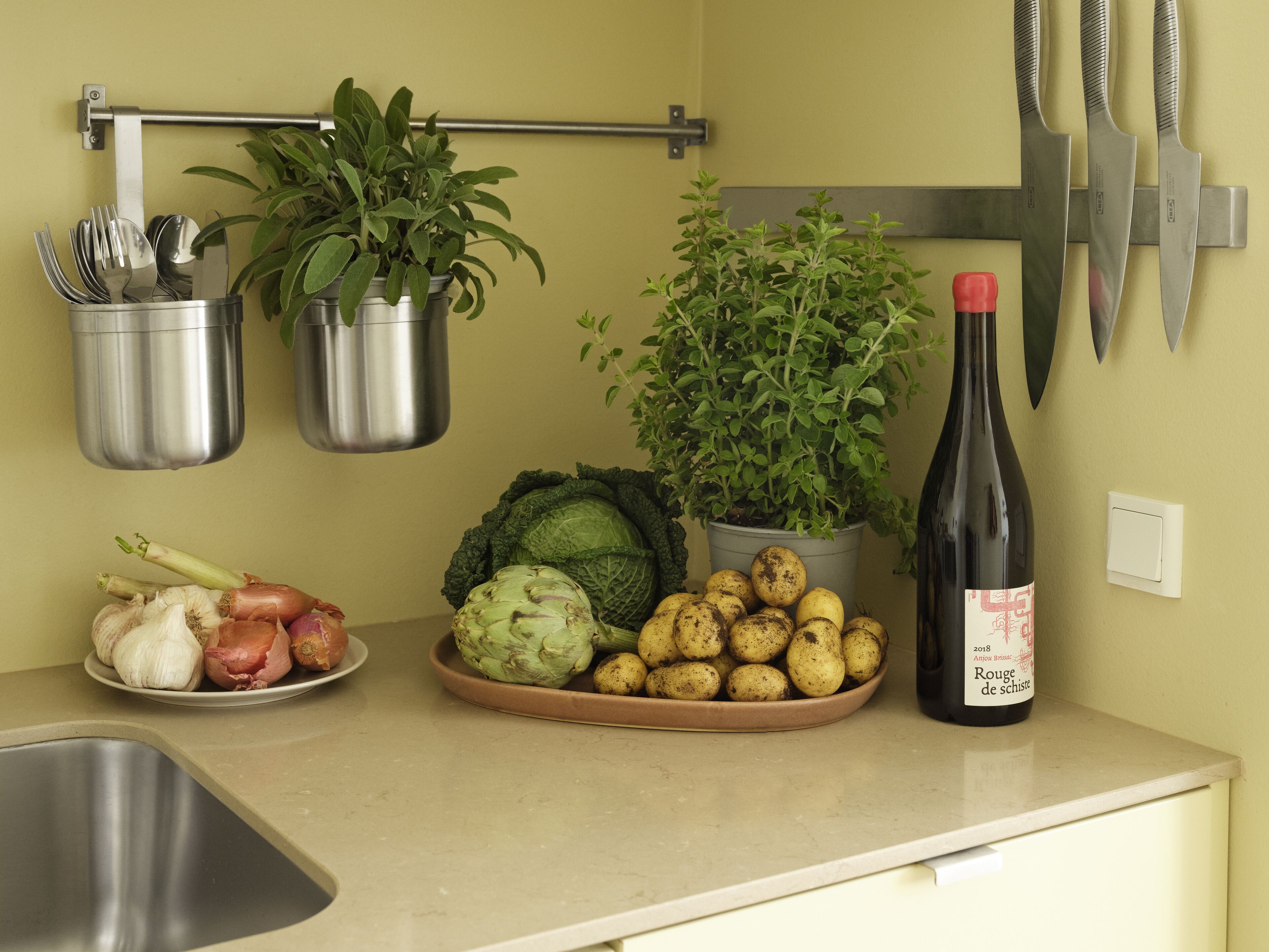 A kitchen counter with a sink, a plate of vegetables, a bottle of wine, and hanging utensils.