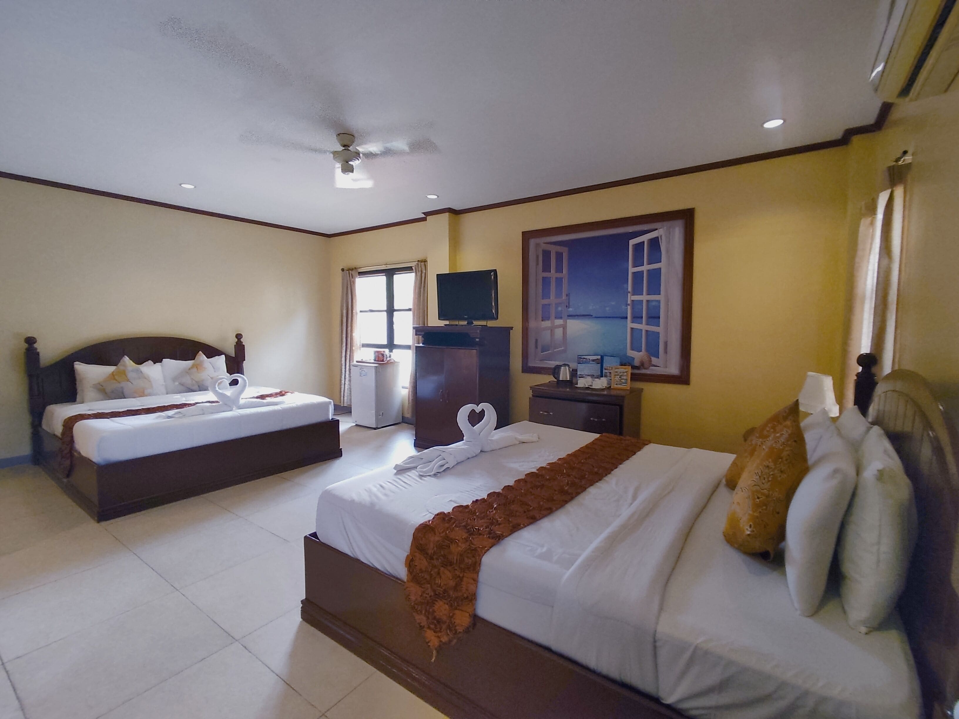Habitación de hotel con dos camas, televisión, escritorio y un cuadro con vista al mar.