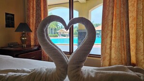 Une chambre d’hôtel avec un lit, une lampe et une vue sur une piscine, visible à travers une fenêtre munie de rideaux.