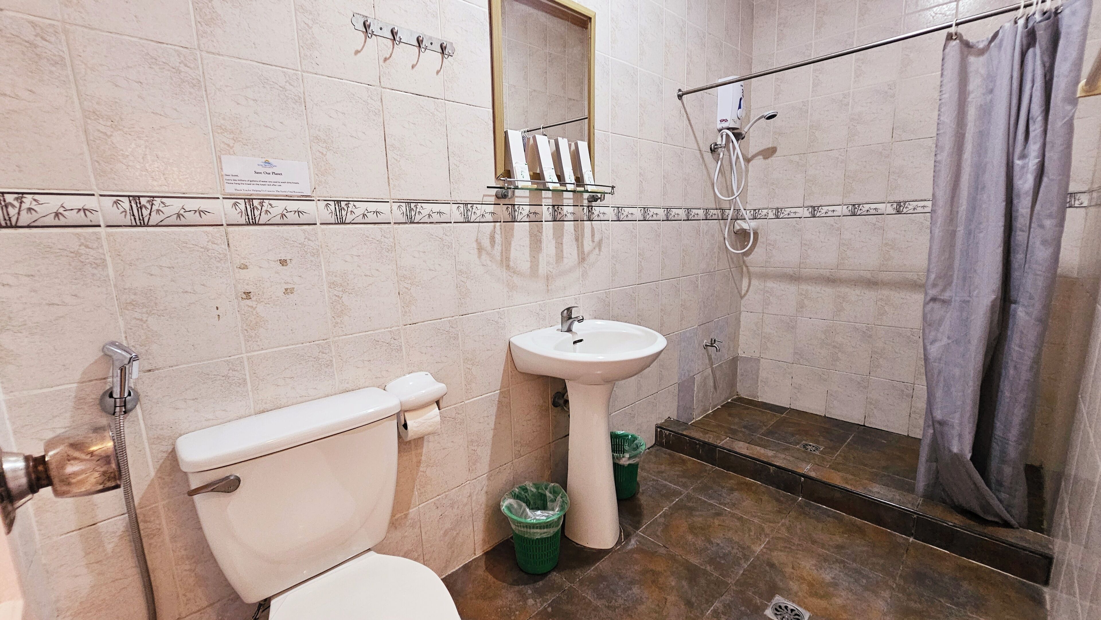 Een badkamer met toilet, wastafel en douche. Handdoeken en een prullenbak zijn aanwezig.