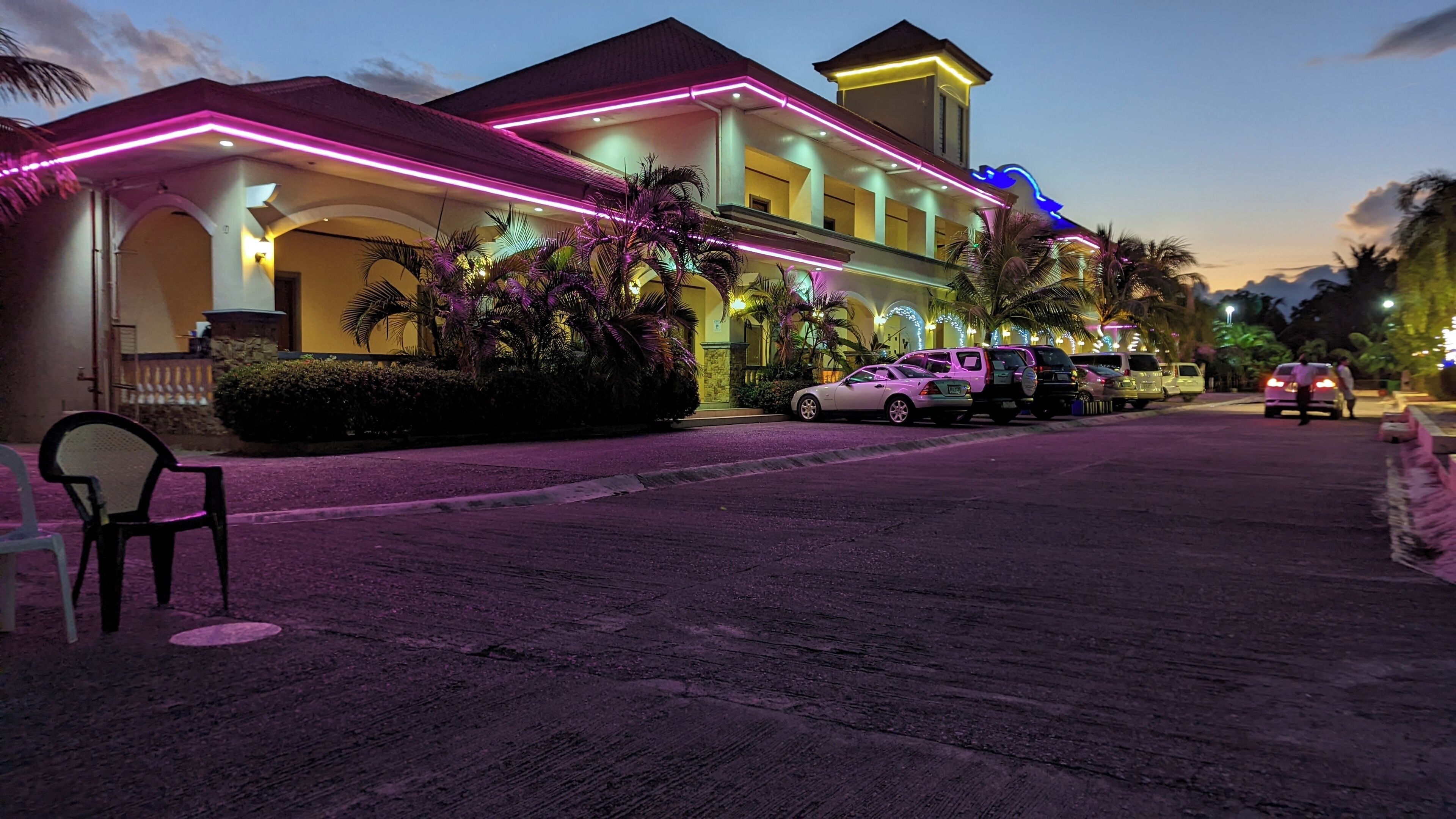 A hotel with a modern design, featuring a prominent entrance with neon lights and a well-maintained outdoor area with parked cars and palm trees.
