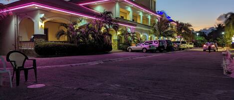 A hotel with a modern design, featuring a prominent entrance with neon lights and a well-maintained outdoor area with parked cars and palm trees.