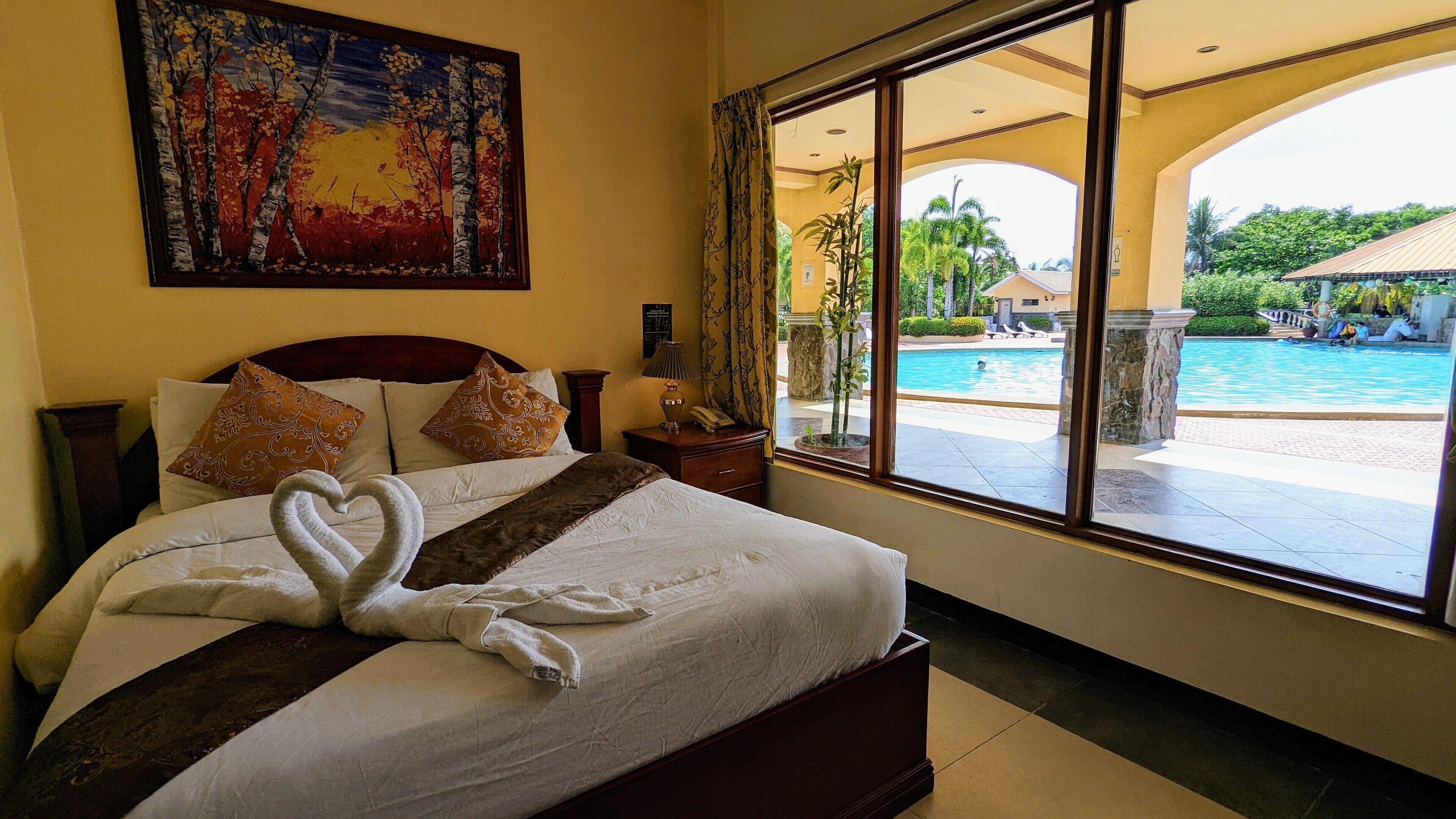 Ein Hotelzimmer mit einem großen Bett, einem Gemälde an der Wand und Blick auf einen Pool.