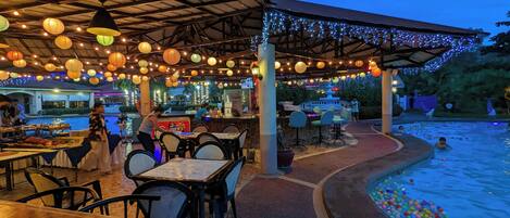 An outdoor dining area with tables and chairs, a pool with colorful balls, and a covered seating area with string lights.