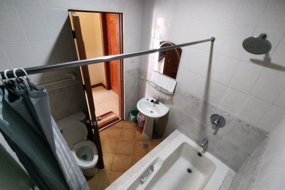 A bathroom with a toilet, sink, and bathtub. There is a showerhead on the wall and a towel rack.